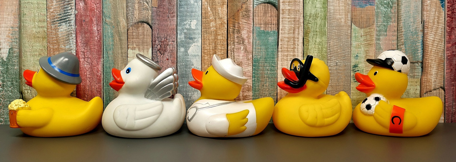 Five rubber ducks, each with different decorations, lined up behind each other