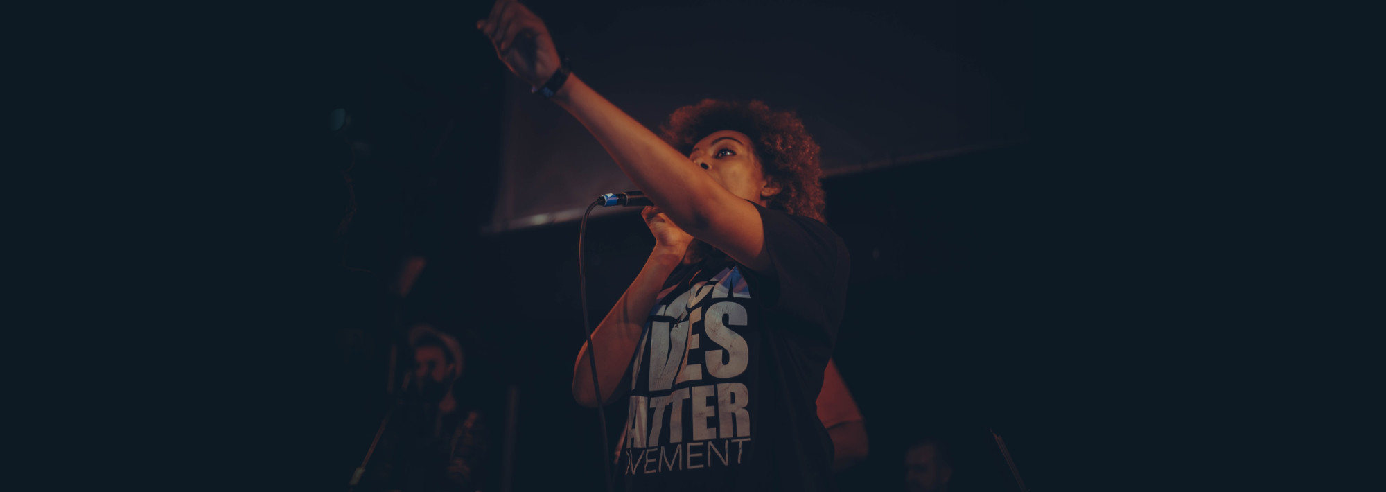 A women with a Black Lives Matter t-shirt speaking into a microphone.