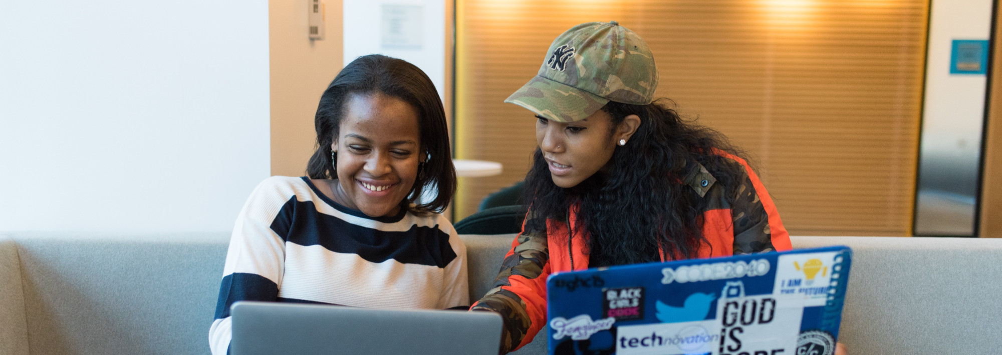 Two Black women with laptops working together.