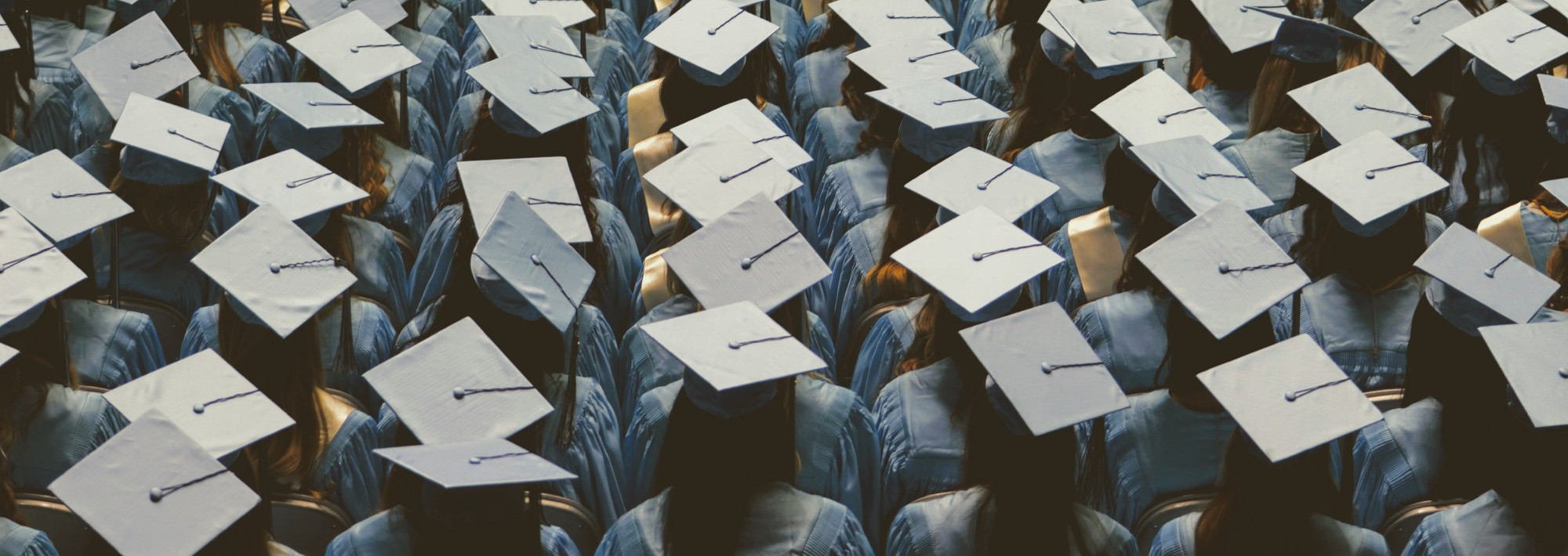 Multiple rows of students sitting, wearing graduation caps and gowns.