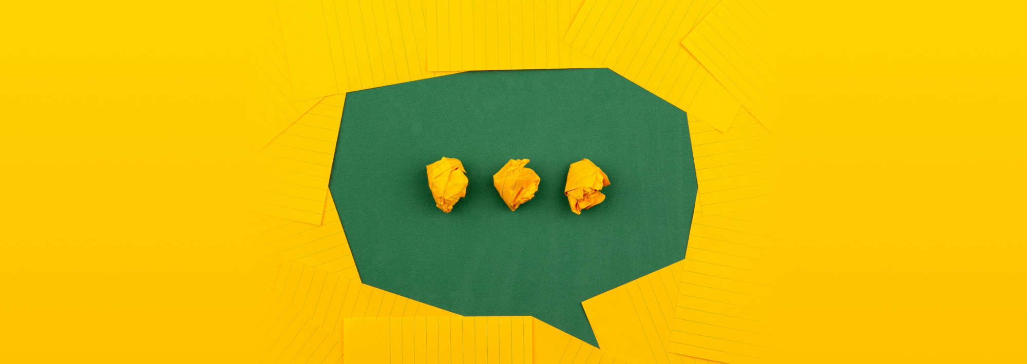 Orange sheets of paper lie on a green school board and form a chat bubble with three crumpled papers.