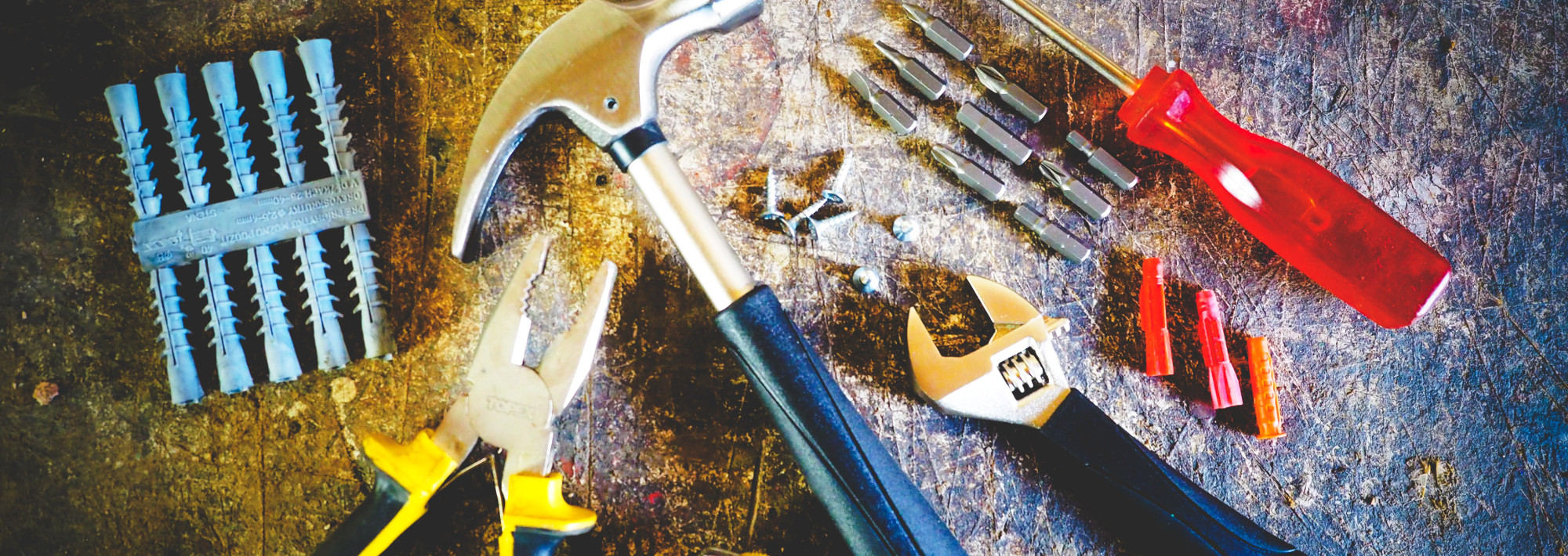 An assortment of tools, like a hammer, plier and a wrench, lying on a wooden table.